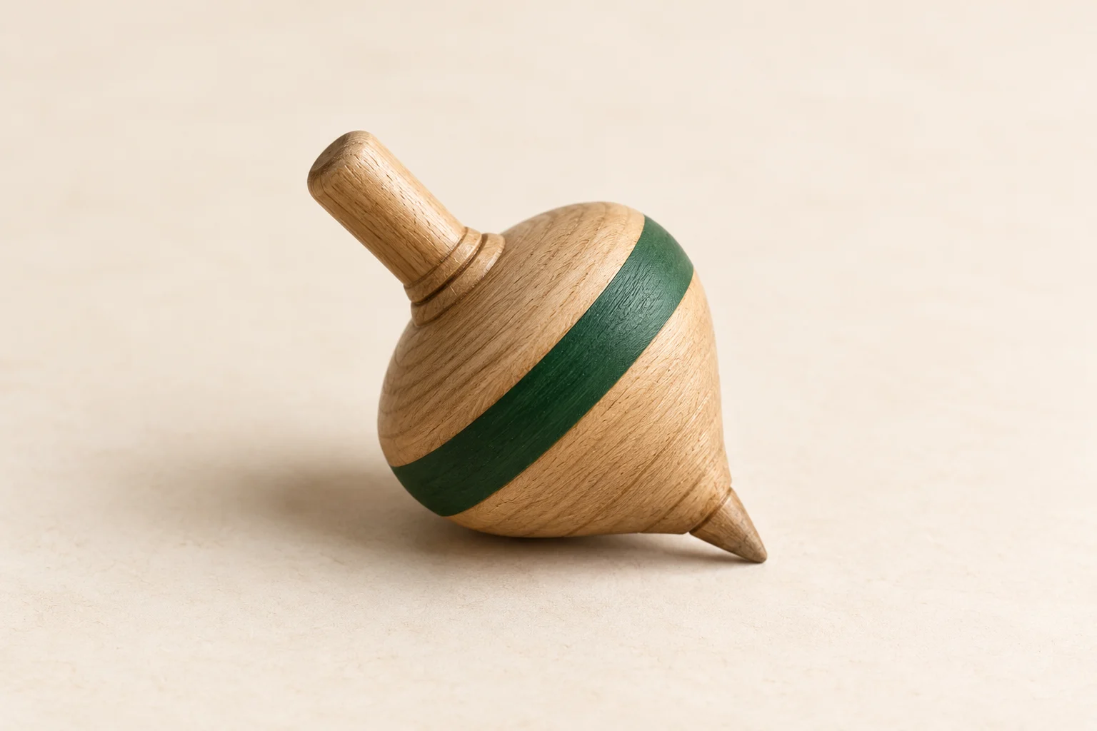 Illustrative wooden spinning top resting on its side, with a deep-green band around its body on an ivory surface